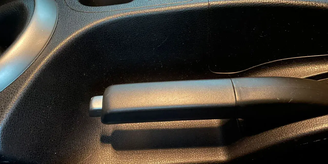 Maniglia del freno di servizio in un'auto, con portabicchieri e pulsante di blocco nelle vicinanze.