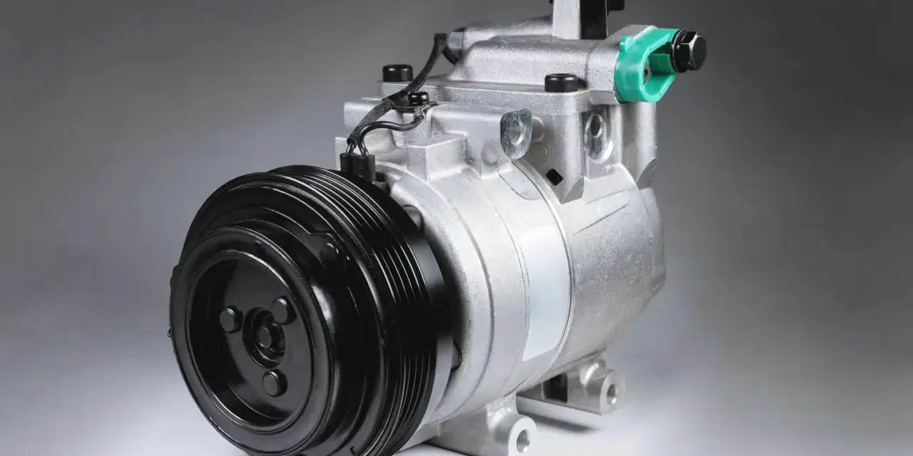 Compressore d'aria condizionata auto: scopri come funziona. Componente metallico argentato con puleggia nera.