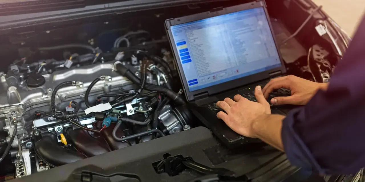 Meccanico controlla il motore di un'auto con un laptop, analizzando dati per ottimizzare l'anticipo automatico motori diesel.
