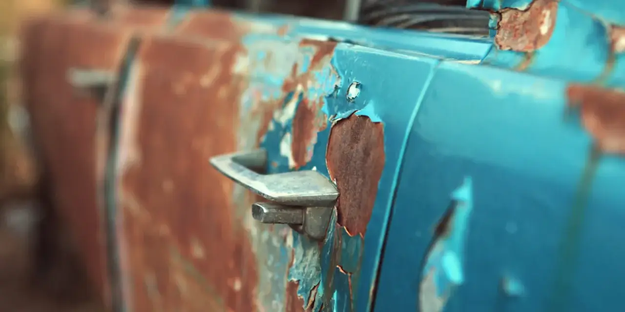 Portiera di un'auto blu con vernice scrostata e ruggine evidente. Un lavoro di restauro per togliere la ruggine sarebbe necessario per riportarla al suo antico splendore.