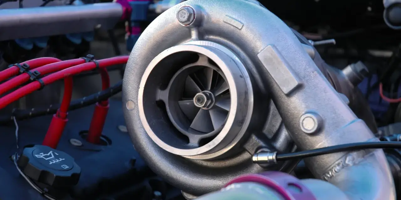 Dettaglio di un motore con un turbo benzina cromato, cavi rossi e un tappo dell'olio.