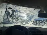 Vetro dell'auto coperto di brina, con segni di tergicristallo. Un sole pallido filtra attraverso il ghiaccio, rendendo difficile vedere. Ecco come sbrinare il vetro della macchina.