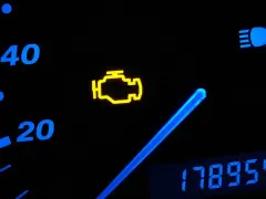 Cruscotto auto con spia motore accesa, indicatore di velocità e chilometraggio.