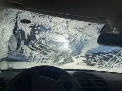 Vetro dell'auto coperto di brina, con segni di tergicristallo. Un sole pallido filtra attraverso il ghiaccio, rendendo difficile vedere. Ecco come sbrinare il vetro della macchina.