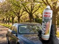 Mano guantata tiene spray MAFRA Resin Off per rimuovere resina e lucidare la plastica dell'auto, con auto scura sullo sfondo.
