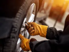 Mani guantate stringono bulloni ruota auto, seguendo la tabella coppia serraggio per sicurezza.