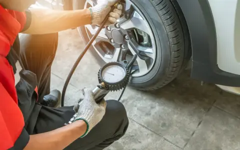 Controllo pressione gomme: il manometro indica pressione gomme troppo alta. Un meccanico con guanti sta verificando la pressione di un pneumatico.