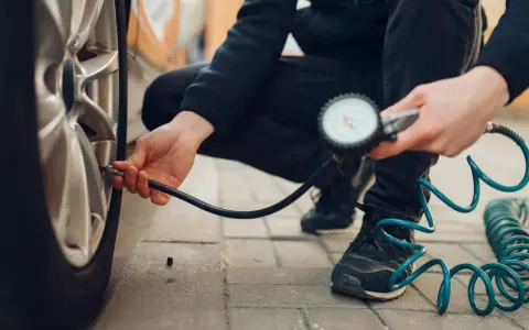 Persona controlla la pressione degli pneumatici dell'auto con un manometro, seguendo la tabella pressione pneumatici auto per la sicurezza.