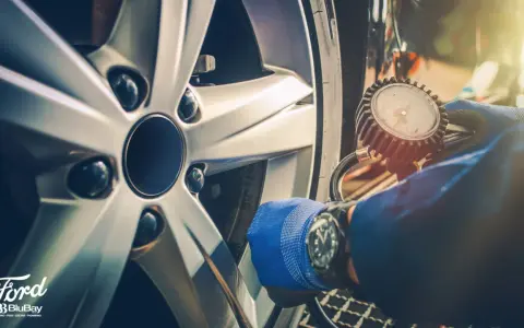 Controllo pneumatici con manometro su cerchio Ford. Guanto blu e orologio da polso.
