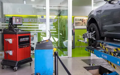 Attrezzatura per la convergenza gomme in officina. Un'auto è sollevata su un ponte, con sensori applicati alla ruota.