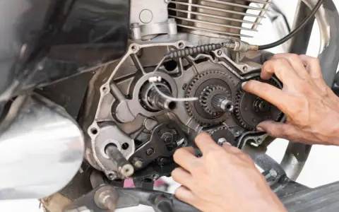 Mani che lavorano sul cambio di una moto, forse per risolvere una perdita di potenza auto benzina. Ingranaggi e meccanismi a vista.