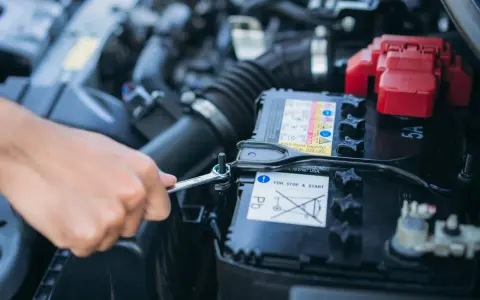 Mano con chiave inglese che lavora sulla batteria dell'auto. La batteria si scarica a vettura ferma, un problema comune per le auto con sistema Start & Stop.