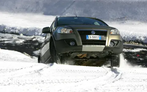 Un'auto con gomme invernali neve affronta un pendio innevato, sollevando spruzzi di bianco.