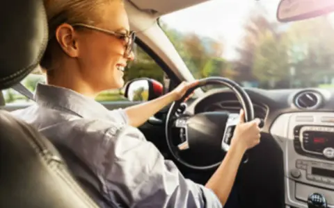 Donna sorridente guida con il volante che vibra a bassa velocità, godendosi il sole del mattino.