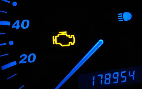 Cruscotto auto con spia motore accesa, indicatore di velocità e chilometraggio.