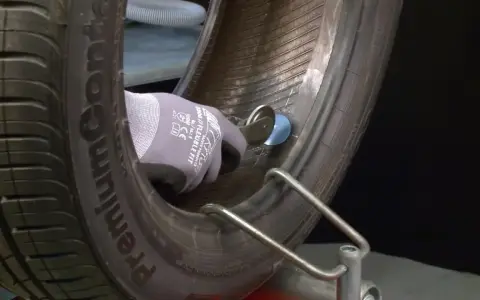 Mano guantata che esegue la riparazione gomma con un attrezzo, fissando una toppa interna.