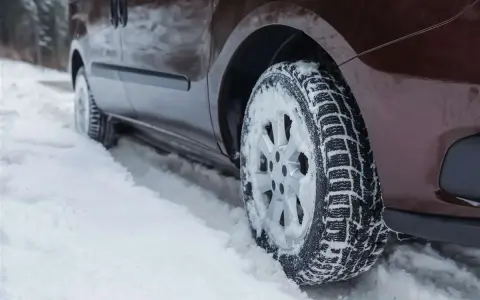 Un'auto marrone avanza su una strada innevata, le ruote dotate di pneumatici chiodati per affrontare il ghiaccio e la neve.