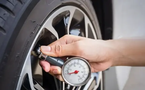Controllo della pressione gomme 185/65 r15 con manometro. La mano tiene lo strumento attaccato alla valvola.