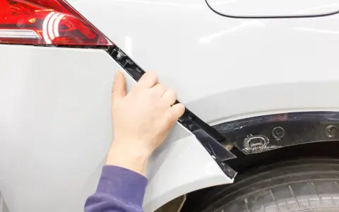 Mano che lavora alla riparazione paraurti in plastica di un'auto bianca.