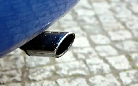 Il tubo di scarico cromato di un'auto blu, parte del silenziatore che attutisce il rumore del motore, su un selciato.
