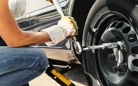 Persona con guanti gialli usa una chiave per serrare i bulloni della ruota di un'auto sollevata da un cric. Il significato di "nm" è la coppia di serraggio.
