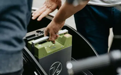 Mani che inseriscono una batteria verde in un vano. La durata della batteria della macchina è fondamentale per l'autonomia.