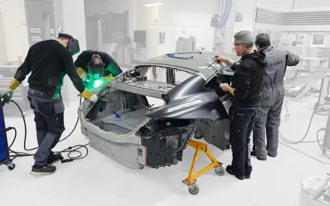 Operai saldano il telaio macchina in officina. Uno di loro usa una saldatrice, mentre gli altri osservano e lavorano sulla carrozzeria.