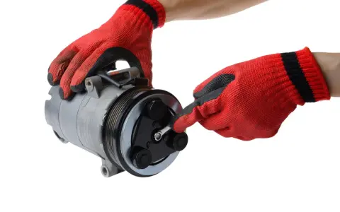 Mani guantate rosse lavorano su un compressore per la sostituzione del compressore aria condizionata auto.