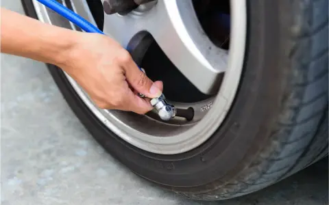 Mano che collega un tubo blu alla valvola di un pneumatico per controllare la pressione gomme auto.