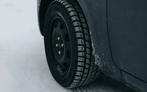 Ruota di un'auto con pneumatico invernale coperto di brina, pronto per affrontare la neve. La scheda pneumatici è fondamentale per la sicurezza.