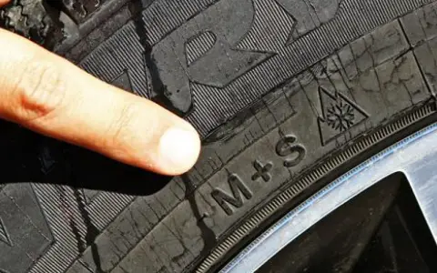 Dito indice indica il simbolo del fiocco di neve su un battistrada gomme invernali M+S, pronto per la neve.