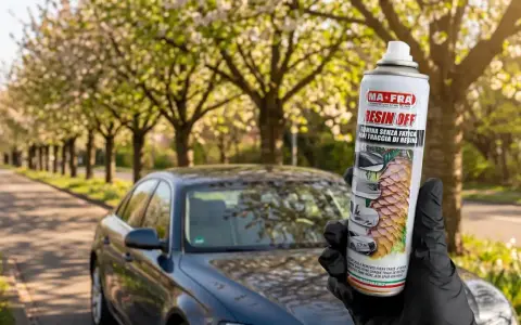 Mano guantata tiene spray MAFRA Resin Off per rimuovere resina e lucidare la plastica dell'auto, con auto scura sullo sfondo.