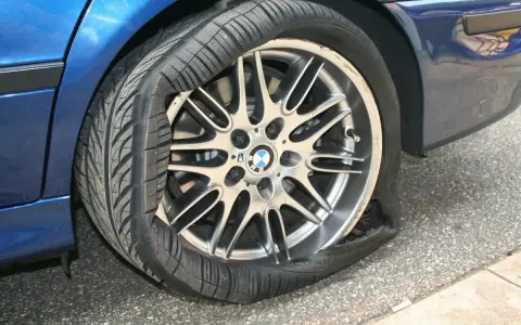Un pneumatico squarciato sul cerchione di un'auto blu. La gomma è completamente sgonfia e deformata, mostrando il danno.