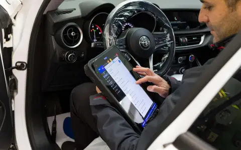 Meccanico usa tablet per diagnosticare la centralina auto. Il dispositivo mostra le opzioni di controllo e i dati del veicolo.