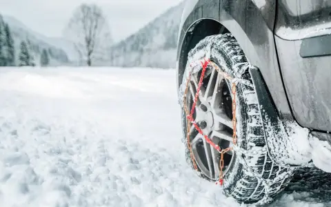 Ruota di un'auto con catene da neve su una strada innevata. Per affrontare la neve, quante catene da neve servono? Di solito due, una per ogni ruota motrice.