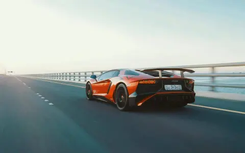 Arancia Lamborghini sfreccia su un ponte, i suoi cavalli scatenati sull'asfalto. L'auto sportiva domina la scena, un'icona di velocità.