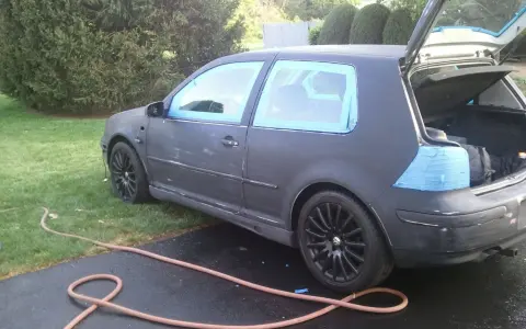 Auto grigia con nastro blu sui finestrini, pronta per la vernice per auto a rullo. Tubo da giardino sul vialetto.