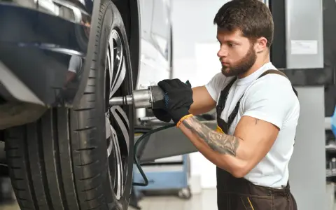 Meccanico con guanti neri lavora su una ruota. Per sapere ogni quanto girare le gomme, consulta il manuale dell'auto.
