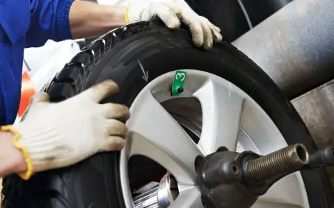 Tecnico con guanti esegue equilibratura gomme per eliminare vibrazioni. Ruota su macchinario specifico.