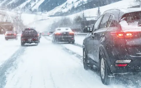 Auto con trazione posteriore sulla neve, luci accese, in un paesaggio montano innevato.