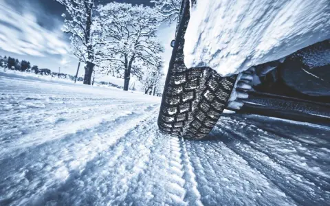 La gomma ghiaccio affronta la neve su una strada invernale, lasciando profonde tracce. Alberi innevati sullo sfondo.
