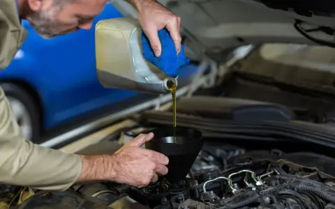 Meccanico versa olio motore da una tanica in un imbuto, risolvendo una perdita olio motore lato destro.