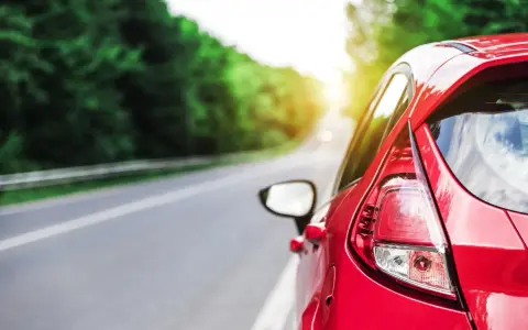 Auto rossa in accelerazione su strada panoramica, con il sole che filtra tra gli alberi.