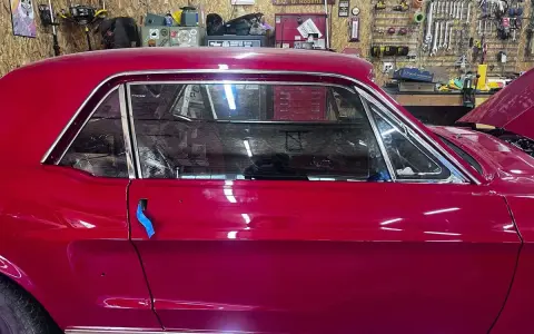 Auto d'epoca con vernice rosso candy apple lucida, in un garage con attrezzi appesi.