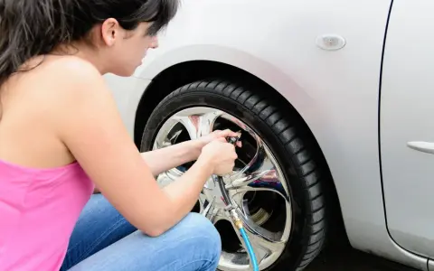 Donna in jeans e canotta rosa usa un compressore per gonfiare le gomme dell'auto, assicurandosi che siano alla pressione giusta.