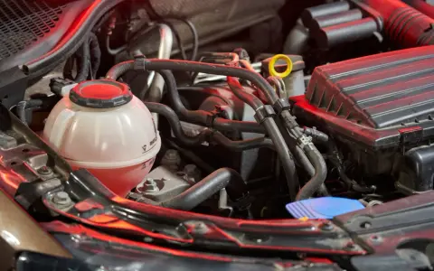 Serbatoio trasparente con liquido rosso, parte dell'impianto di raffreddamento del motore, circondato da tubi e componenti meccanici.