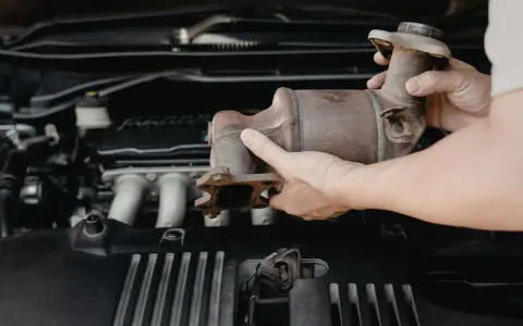 Mani che rimuovono un catalizzatore arrugginito dal vano motore di un'auto. Riparazione del fap auto.