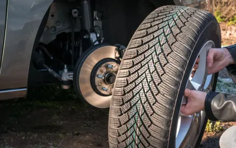 Mani che montano una gomma nuova su un cerchio, con il mozzo dell'auto visibile. La rotazione gomme auto è fondamentale per l'usura uniforme.