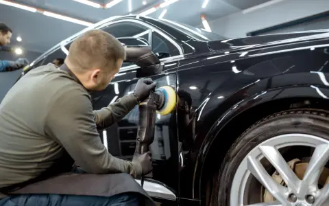 Dettaglio di un professionista che lucida una carrozzeria metallizzata nera per eliminare graffi, con lucidatrice rotativa.