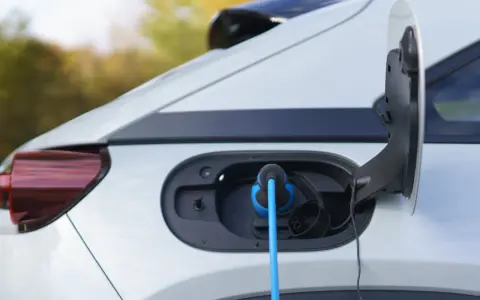 Auto elettrica in carica, con cavo blu collegato alla porta. La coppia motore è pronta per la prossima avventura.